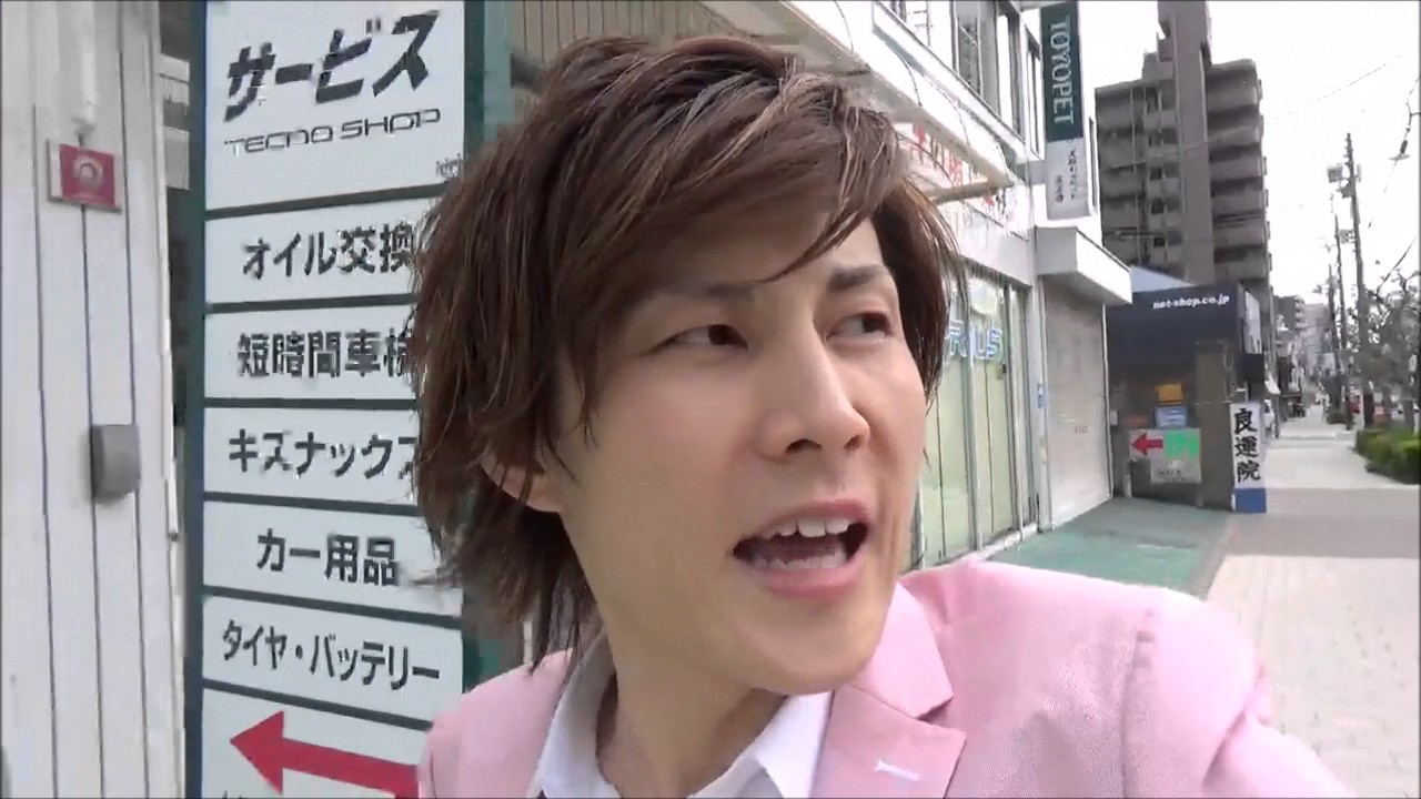 商店街の看板前を歩きながら話す本人(バイクは都心で機能しない)(動画「バイクを売る理由」より)