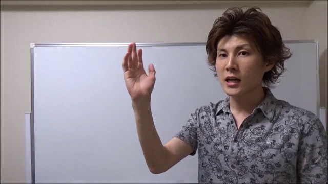 ホワイトボード前で柄シャツ姿の本人が片手を挙げて話す(動画「サラリーマンをクビにしました【スロプロ】…」より)