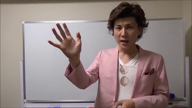 ホワイトボード前で手を広げて話す本人(動画「人を見極めよう」より)