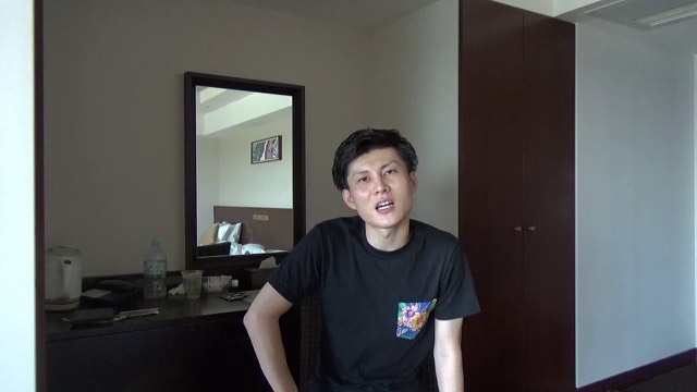 ホテルの一室で黒Tシャツ姿の本人が話す(動画「【貧困時代】お金がなくてキツい理由」より)