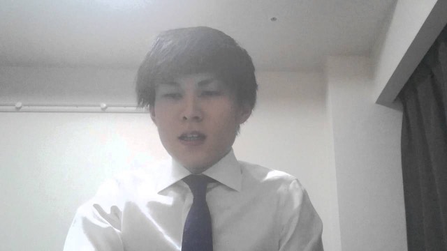 白シャツ・ネクタイ姿で逆光気味に立つ本人(動画「質問 パチスロのガックンとは何ですか?」より)