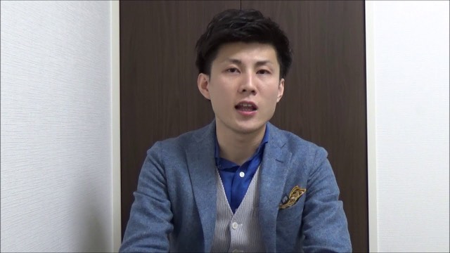 青いブレザーにポケットチーフの本人(動画「パチスロ、スロットで勝つスロプロ ライバル対策」より)