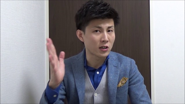 青いブレザーにポケットチーフの本人(木目扉背景)(動画「パチスロ、スロットで勝つスロプロ モデリングしよう」より)