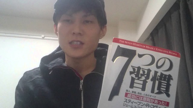 キャップを被り書籍「7つの習慣」を掲げる本人(動画「7つの習慣について ※パチスロと関係ないです」より)