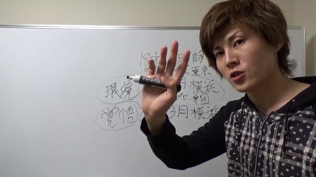 ホワイトボードの地名・日付メモを指す本人(動画「スロットで稼げるようになるまでの流れ」より)