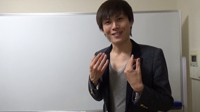 黒ジャケット姿で笑いながらホワイトボード前に立つ本人(動画「初心者向け パチスロで稼いで生活する人 【パチスロ】」より)