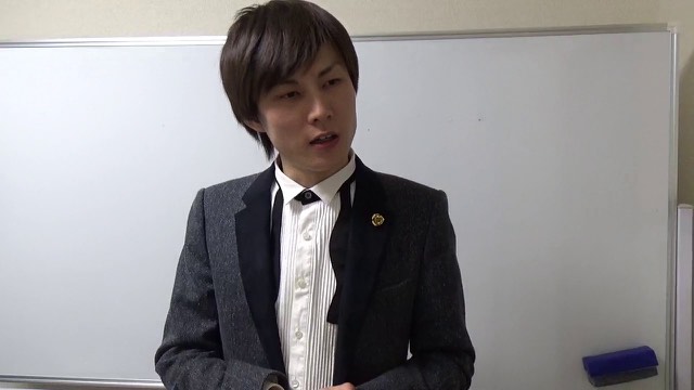 グレージャケット姿でホワイトボード前に立つ本人(動画「自分で決める【パチスロ】【スロット】」より)