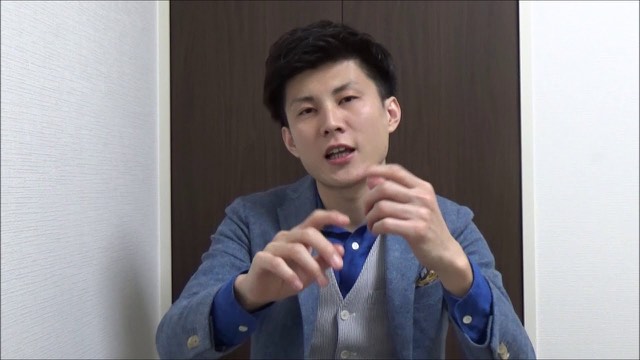ベスト・グレージャケット姿で両手を動かしながら話す本人(動画「パチスロ、スロットで勝つスロプロ 目押しができない」より)