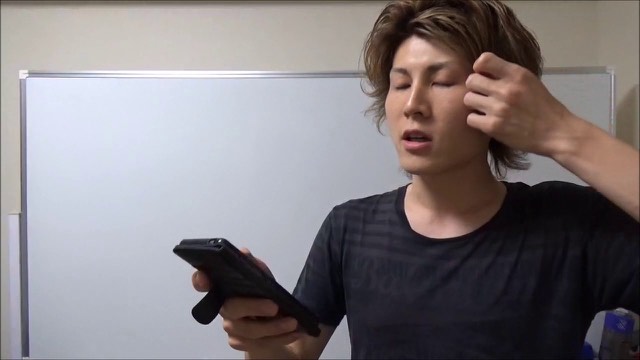 スマホを持ち目を閉じてこめかみに手を当てる本人、ホワイトボード背景(動画「Twitterで夏目五郎を検索するとアツイ…」より)
