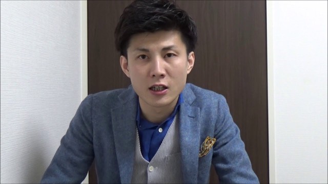 ベスト・ジャケット姿で扉を背景に話す本人(動画「ネットビジネス、起業で成功するコツ 詐欺ではなくレバ」より)