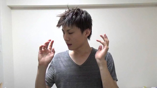 無地の白背景でグレーのVネックを着て両手を動かす本人(動画「結果が出ない人の共通点【パチスロ】【スロット】」より)