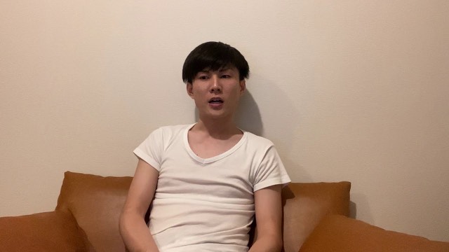 無地の壁を背景に白いTシャツでソファに座り話す本人(動画「無料で何でも提供しても自分が苦しくなるだけ」より)