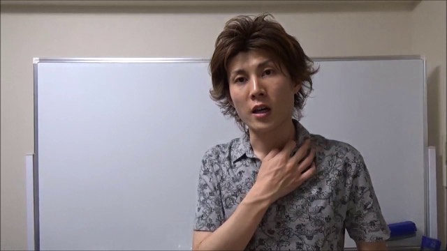ホワイトボード前で胸に手を当てて話す柄シャツ姿の本人(動画「Facebookやってますか?【スロプロ】…」より)